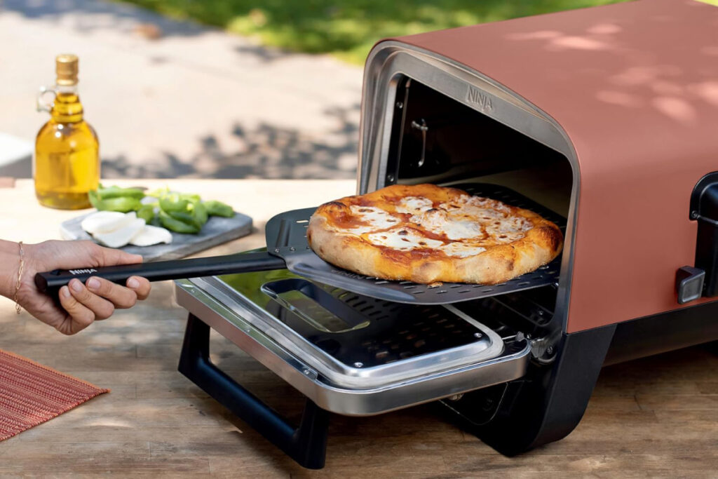 Ninja OO101 Woodfire Outdoor Pizza Oven showcasing its sleek design and powerful cooking capabilities in a backyard setting, perfect for home pizza enthusiasts.